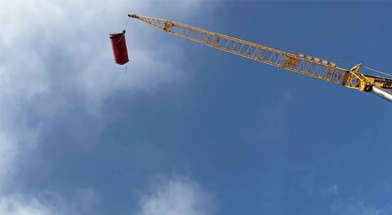 High-reach mobile crane performing a specialized heavy lift of a red industrial tank against a partly cloudy sky.