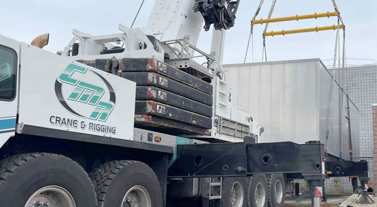 All-terrain mobile crane with CMR logo and counterweights executing a precision heavy lift at a facility.