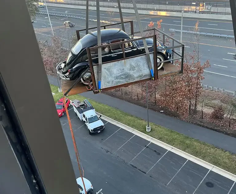 CMR Crane and Rigging hoisting a classic black Volkswagen Beetle in a rigging platform outside a building in Arlington, Virginia.