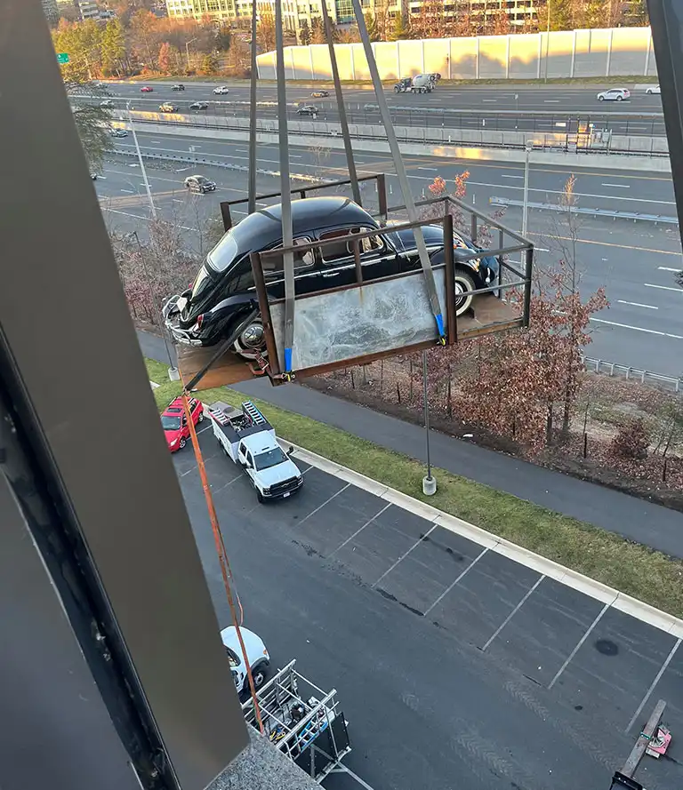 CMR Crane and Rigging hoisting a classic black Volkswagen Beetle in a rigging platform outside a building in Arlington, Virginia.